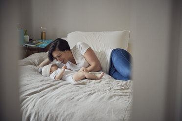 Happy mother looking at son while lying on bed at home - CAVF57693