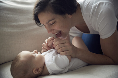 Glückliche Mutter spielt mit ihrem Sohn, der zu Hause auf dem Sofa liegt, lizenzfreies Stockfoto