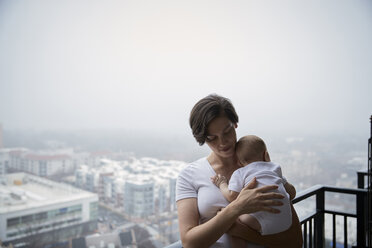 Mutter trägt ihren Sohn bei nebligem Wetter auf dem Balkon - CAVF57704
