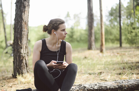 Frau hört Musik, während sie auf einem Feld im Wald sitzt, lizenzfreies Stockfoto