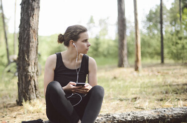 Woman listening music while sitting on field in forest - CAVF57708