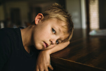 Portrait of serious boy lying head on table at home - CAVF57726