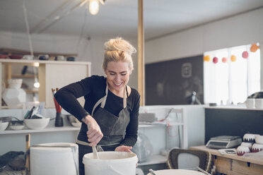 Smiling woman mixing paint in workshop - CAVF57758