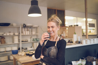 Lächelnde Frau, die in der Werkstatt steht und etwas trinkt - CAVF57766