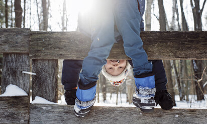Porträt eines glücklichen Jungen, der sich im Winter auf einem Zaun stehend bückt - CAVF57771