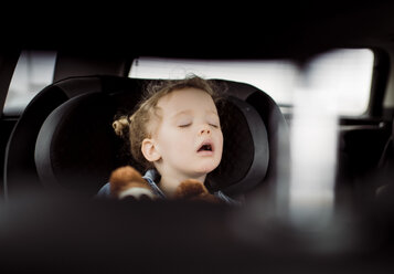 Cute girl with mouth open sleeping in car seen through vehicle seat - CAVF57774