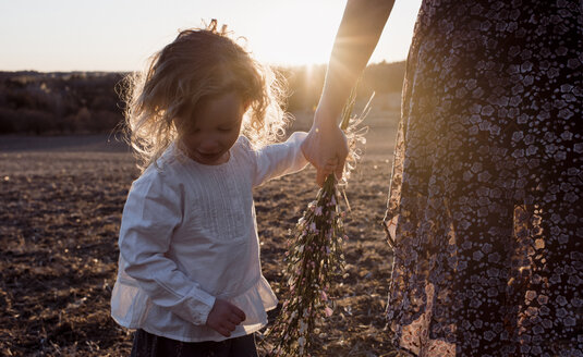 Mittelteil einer Mutter, die die Hand ihrer Tochter hält, während sie bei Sonnenuntergang auf einem Feld steht - CAVF57779