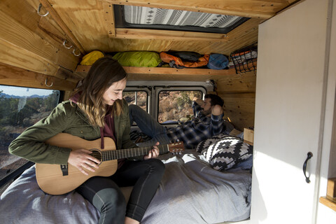 Frau spielt Gitarre, während sie mit einem Freund im Wohnmobil sitzt, lizenzfreies Stockfoto