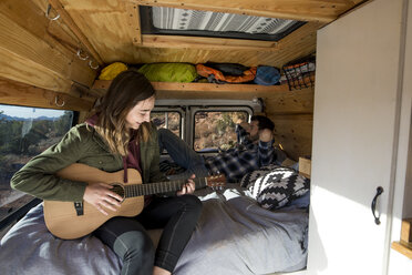 Frau spielt Gitarre, während sie mit einem Freund im Wohnmobil sitzt - CAVF57784