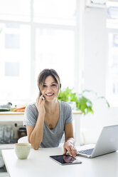 Happy oman sitting at desk, working from home, using laptop - MOEF01710