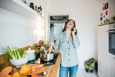 Laughing woman talking on the phone, while preparing pumpkin soup - MOEF01716