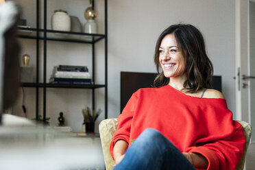 Happy woman wearing a red pullover, sitting in her living room - MOEF01723