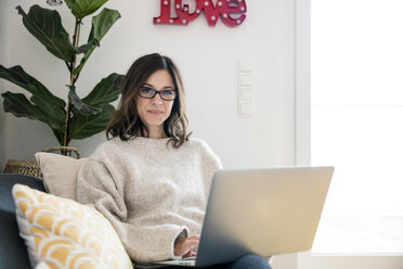 Woman sitting on her couch, surfing the net, using laptop - MOEF01732