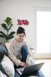 Woman sitting on her couch, surfing the net, using laptop - MOEF01733