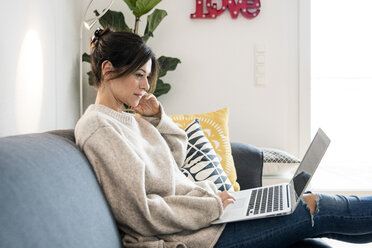 Frau sitzt auf ihrer Couch, surft im Internet und benutzt einen Laptop - MOEF01735