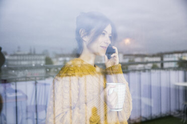 Frau steht am Fenster, trinkt Tee, telefoniert - MOEF01739