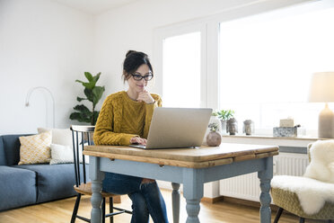 Frau sitzt am Tisch und benutzt einen Laptop - MOEF01744