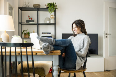 Woman sitting at table with feet up, using laptop - MOEF01747