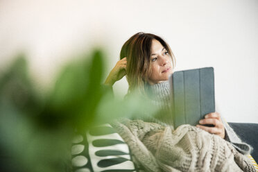 Frau auf der Couch sitzend, in eine Decke gehüllt, E-Book lesend - MOEF01748