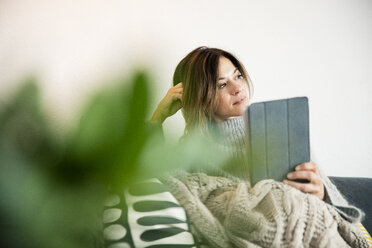 Woman sitting on couch, wrapped in a blanket, reading e-book - MOEF01748