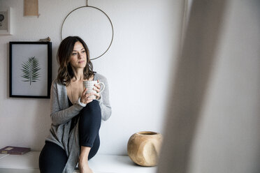 Woman sitting on chest of drawers, drinking tea, relaxing - MOEF01753