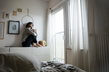 Woman sitting on chest of drawers, drinking tea, relaxing - MOEF01754