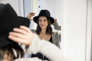 Mature woman standing in front of mirror , putting on a hat - MOEF01756