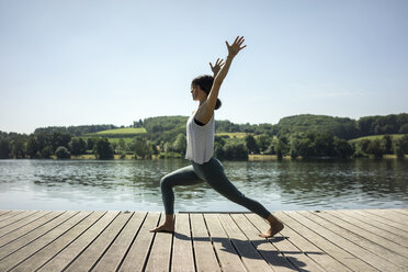 Mature woman practicing yoga in summer on a jetty at a lake - MOEF01761