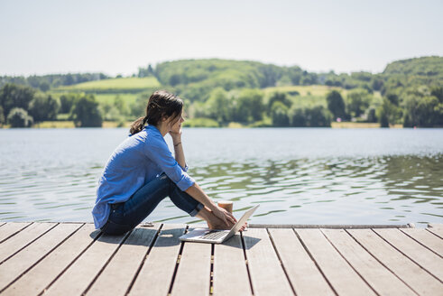Ältere Frau sitzt auf einem Steg an einem See und macht eine Pause - MOEF01779