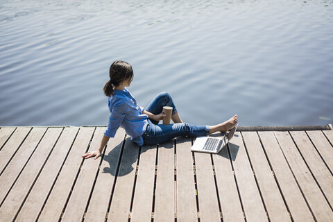 Ältere Frau sitzt auf einem Steg an einem See und macht eine Pause, lizenzfreies Stockfoto