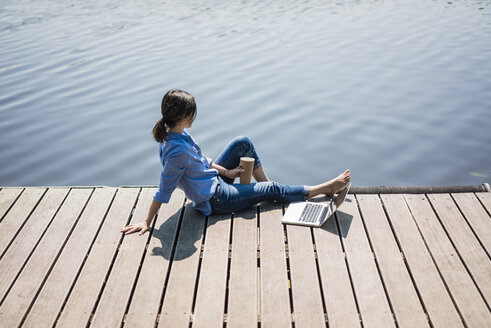 Ältere Frau sitzt auf einem Steg an einem See und macht eine Pause - MOEF01780