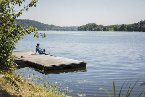 Mature woman sitting on a jetty at a lake, taking a break - MOEF01781