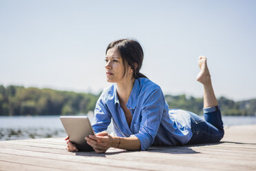 Mature woman working at a lake, using digita tablet on a jetty - MOEF01785