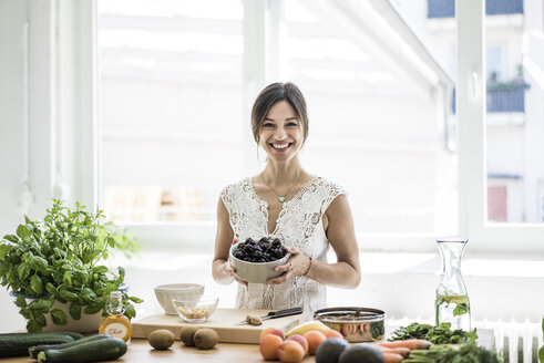 Woman preparing healthy food in her kitchen, holding bowl of cherries - MOEF01789