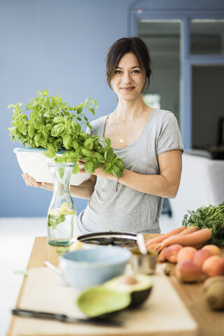 Frau steht in der Küche und hält einen Topf mit Basilikum, lizenzfreies Stockfoto