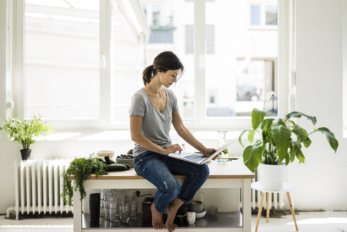 Woman sitting on kitchen table, searching for healthy recipes, using laptop - MOEF01807