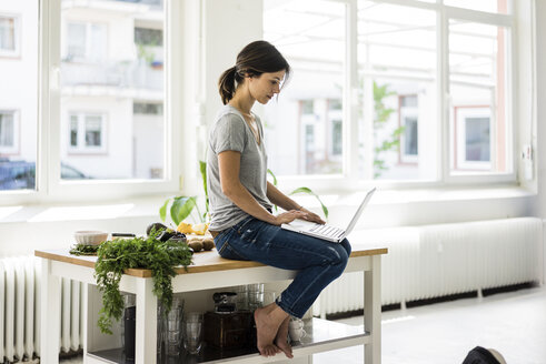 Frau sitzt am Küchentisch, sucht nach gesunden Rezepten und benutzt einen Laptop - MOEF01808
