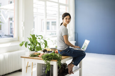 Woman sitting on kitchen table, searching for healthy recipes, using laptop - MOEF01809