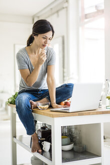 Woman sitting on kitchen table, searching for healthy recipes, using laptop - MOEF01813