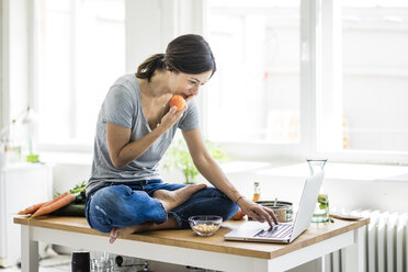 Frau sitzt am Küchentisch, sucht nach gesunden Rezepten und benutzt einen Laptop - MOEF01814