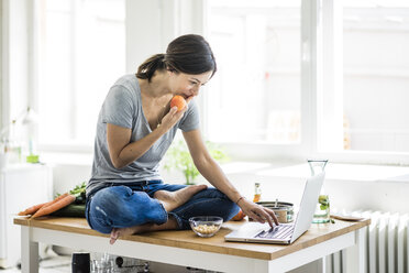 Woman sitting on kitchen table, searching for healthy recipes, using laptop - MOEF01814