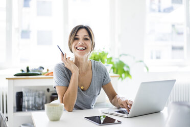 Happy oman sitting at desk, working from home, using laptop - MOEF01819