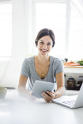 Happy oman sitting at desk, working from home, using laptop - MOEF01822