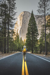 USA, Kalifornien, Yosemite-Nationalpark, Mann geht auf Straße mit El Capitan im Hintergrund - KKAF03032