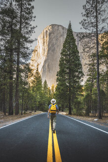 USA, California, Yosemite National Park, man walking on road with El Capitan in background - KKAF03032