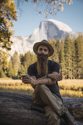 USA, Kalifornien, Porträt eines bärtigen Mannes, der auf einem Baumstamm im Yosemite-Nationalpark sitzt - KKAF03059