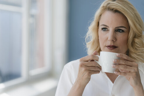 Porträt einer blonden Frau, die am Fenster Kaffee trinkt - KNSF05403