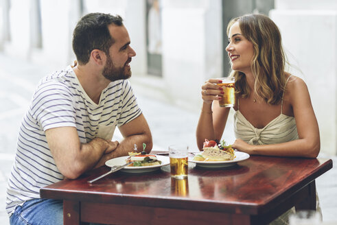Lächelndes Paar beim Essen und Biertrinken in einem Restaurant auf der Straße - JSMF00595