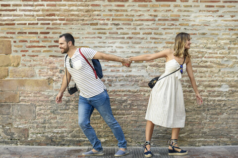 Paar, das sich an den Händen hält und in entgegengesetzte Richtungen an einer Backsteinmauer läuft, lizenzfreies Stockfoto
