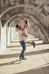 Spain, Andalusia, Malaga, happy man lifting up girlfriend under an archway in the city - JSMF00630